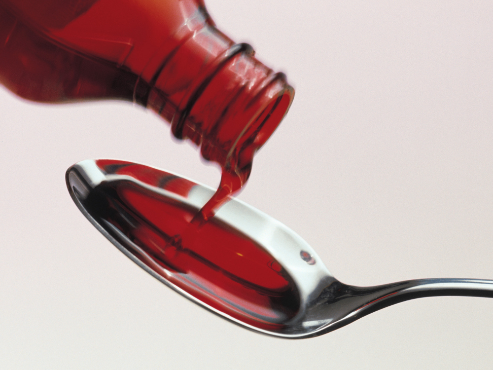 Červený sirup na kašeľ nalievaný z fľaštičky na kovovú lyžičku, používaný na zmiernenie príznakov kašľa.